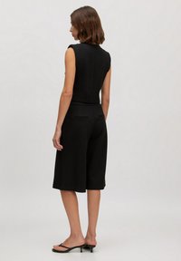 Zwarte mouwloze jumpsuit met wijde shorts, met een getailleerde body en achterzakken. Glad textuur en minimalistisch ontwerp.