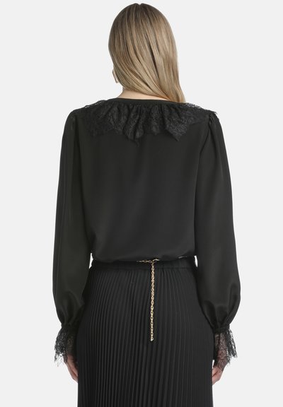 Black blouse with lace-trimmed collar and sleeves. Features a pleated black skirt and a gold chain detail at the waist. Smooth fabric texture.