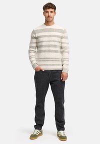 Lys grå genser med horisontale grønne striper, ribbet tekstur, sammen med mørke jeans og grønne sko med hvite striper. Ingen merkbar maskinvare.