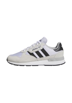 Białe i jasnoszare sneakersy Adidas z czarnymi paskami, zamszowymi nakładkami, sznurowanym designem oraz firmowymi detalami na podeszwie i pięcie.