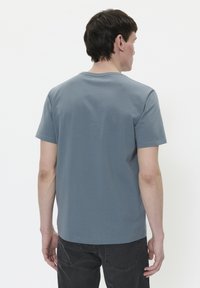 Camiseta gris de manga corta con cuello redondo y una textura suave, vista desde atrás, combinada con jeans oscuros.