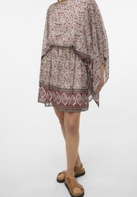 Kukkakuvioinen tunikamekko, jossa on joustava vyötärö, pyöreä pääntie ja väljät, virtaavat hihat hillityissä sävyissä ja yksityiskohtaiset reunukset.