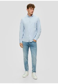 Camicia azzurra chiara con una piccola tasca sul petto, abbinata a jeans azzurri chiari e scarpe da ginnastica bianche. Design semplice e tessuto in cotone.