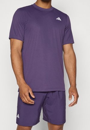 Hombre con camiseta de manga corta y pantalones cortos morados a juego, con pequeños logotipos blancos de Adidas en el pecho y en la pierna izquierda del pantalón corto.