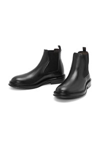 Las botas Chelsea de cuero negro cuentan con paneles elásticos a los lados, lengüetas, punteras redondeadas y una superficie lisa con un ligero tacón.