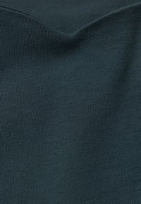 Tumma vihreä, joustava kangas hienolla poimutetulla tekstuurilla, sileästi taitettuna, korostaen sen pehmeää ja hengittävää laatua. Ei näkyviä kuvioita tai tarvikkeita.