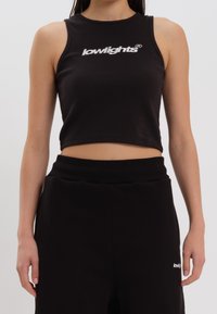 Top corto nero realizzato in materiale a coste, con un logo bianco sulla parte frontale. Abbinato a pantaloni neri a vita alta.