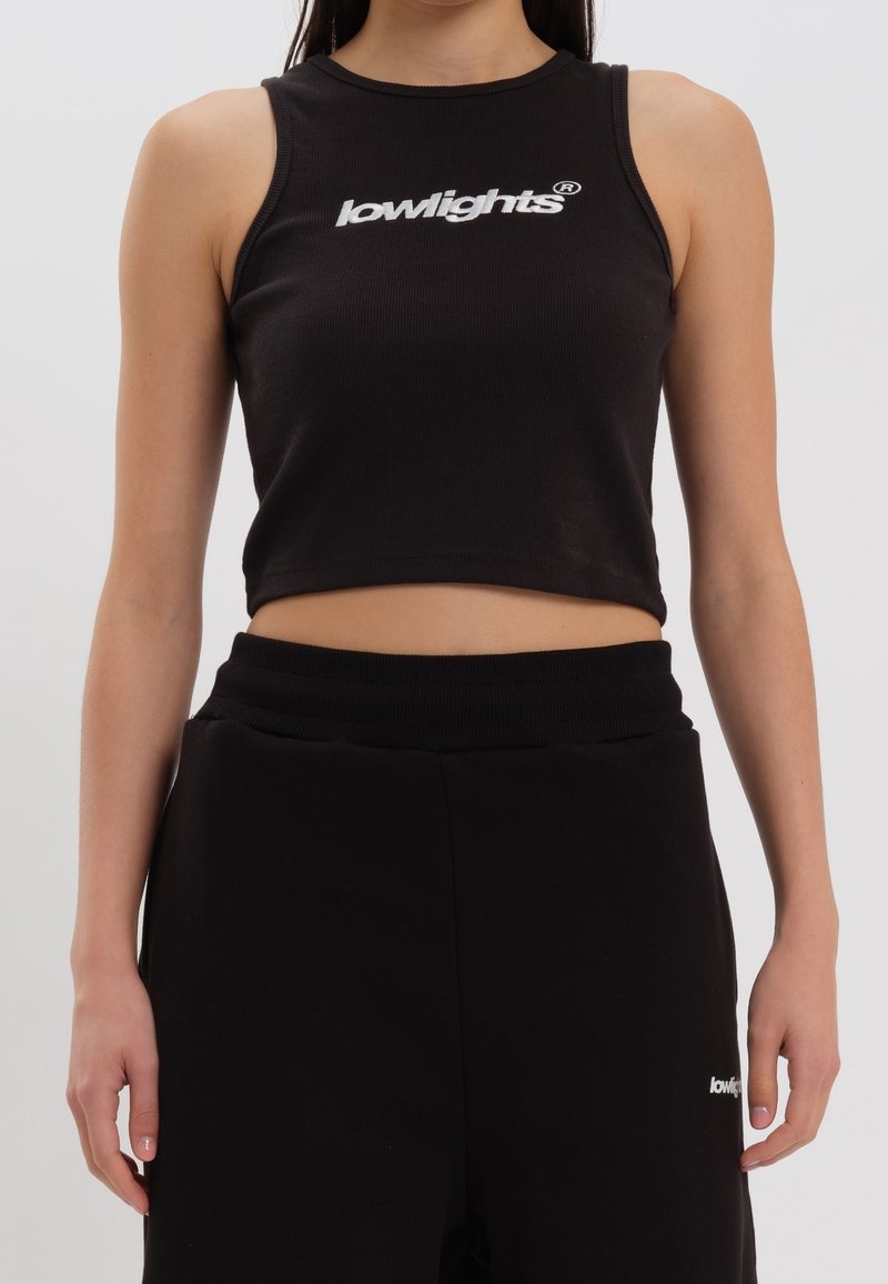 Top corto nero realizzato in materiale a coste, con un logo bianco sulla parte frontale. Abbinato a pantaloni neri a vita alta.