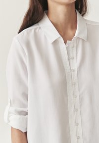 Witte button-up shirt gemaakt van lichtgewicht stof, met een klassieke kraag, een volledige knoopsluiting en opgerolde mouwen.
