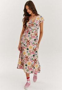 Květinové zavinovací šaty z lehké látky s barevnými vzory, krátkými rukávy a sukní do délky kolen, doplněné růžovými teniskami.