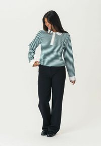 Striped long-sleeve polo shirt in dark green and white with a button placket; paired with black wide-leg trousers and glossy shoes.