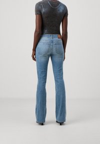 Sittande, ljusblå utsvängda jeans med en subtil tvätt, två bakfickor och en märkesläderpatch vid midjan.