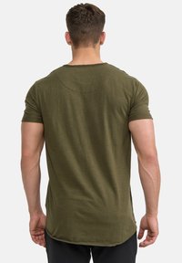 Camiseta de manga corta en verde oliva con cuello redondo, que presenta una costura curva en la parte posterior y un corte relajado, fabricada en suave tejido de algodón.