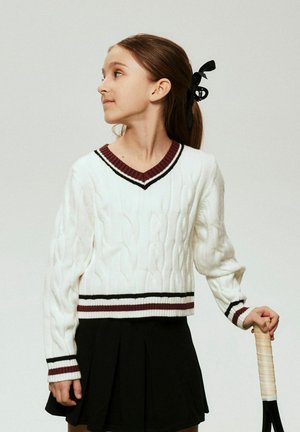 Balts džemperis ar pinuma rakstu un V-veida izgriezumu, ar bordo un melnas svītras akcentiem. Kopā ar melnu krokotu svārku un turot tenisa raketi.