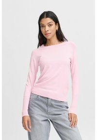 Helles rosa Langarmshirt aus weichem Strickmaterial, mit lockerer Passform und gerippten Bündchen. Kombiniert mit hellgrauen Jeans.