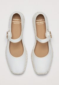Chaussures Mary Jane en cuir blanc avec un bout rond, une sangle réglable avec boucle et une couture de semelle texturée beige. Fabriquées en Espagne.
