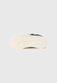Zapatilla negra con suela de goma blanca, con una suela texturizada y parte superior suave. Diseñada para la comodidad con una silueta simple.