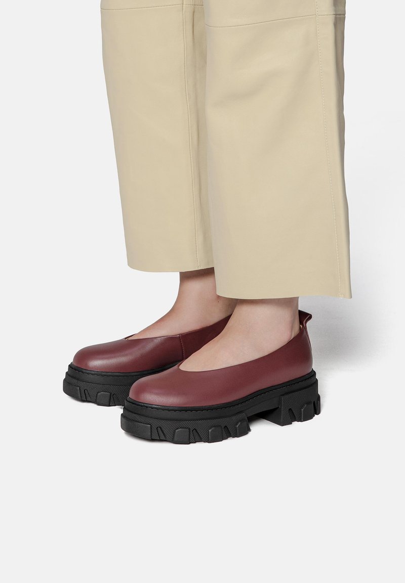 Burgundy leather slip-on shoes with a round toe, featuring a chunky black platform sole and side cutout detail.