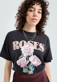 Czarny t-shirt z grafiką z napisem „ROSES” w różowym kolorze, ozdobiony dużym kwiatowym nadrukiem delikatnych różowych róż, z okrągłym dekoltem i krótkimi rękawami.