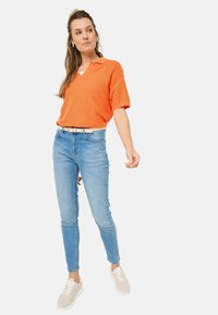 Polo-shirt orange à manches courtes avec une finition texturée, associé à un jean skinny bleu clair et des baskets gris clair.