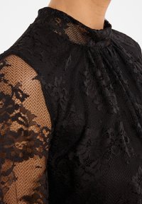 Zwarte kanten top met een hoge halslijn, intrikate bloemmotieven en doorschijnende lange mouwen met geaccentueerde textuur.