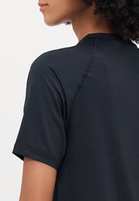Zwarte sportieve t-shirt met korte mouwen, gladde textuur en vlakke naden. Beschikt over een ronde halslijn en zijsplitten voor extra bewegingsvrijheid.