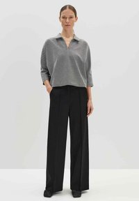 Grijze en zwarte geblokte blouse met een kraag, gedragen met zwarte hoog opgesneden wijde broek met een relaxte pasvorm.