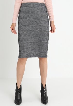 Kvinde iført en grå ternet blyantskørt, lyserød ribbet langærmet top og sorte ankelstøvler med lynlåse foran.