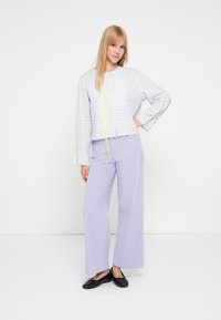 Krótka kurtka w kratę w jasnoszarym kolorze z żółtymi akcentami, zestawiona z szerokimi lawendowymi spodniami o luźnym kroju i fakturowanej tkaninie.