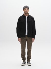 Juoda mygtukais užsegama marškiniai su dviem krūtinės kišenėmis, po apačia balta marškinėlių, smėlio spalvos kelnės ir juodi sportbačiai su baltais padukais. Tvarkingas mezginys kepurė.