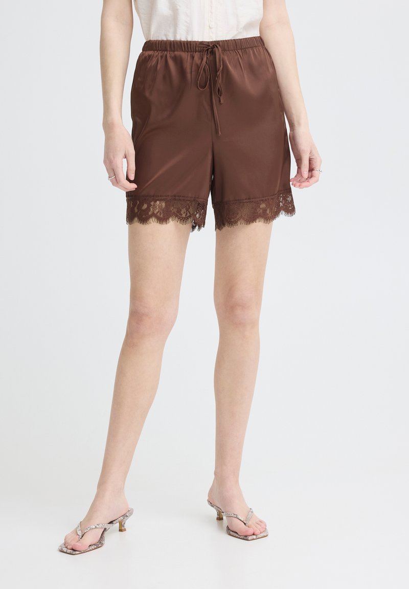 Femme portant un short en satin marron avec un bord en dentelle et une taille à cordon, associé à des sandales à talons de couleur claire.