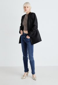 Črn usnjen blazer z dolgimi rokavi, oblečen čez prilegajoč rjav top, v kombinaciji z modrimi ožjimi kavbojkami in kovinskimi visokimi petami.
