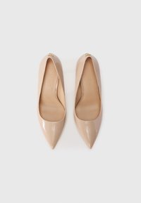 Beige patent leather pointed-toe pumps with an open vamp, featuring a small decorative emblem on the toe area. Smooth texture.