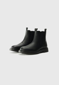 Botas Chelsea de cuero negro con paneles laterales elásticos, punta redonda y acabado texturizado. Cuenta con lengüetas y suela de goma duradera.