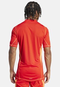 Rode sportieve shirt met korte mouwen, voorzien van een mesh-textuur, contrasterende oranje naden en een geborduurd logo aan de achterzoom.