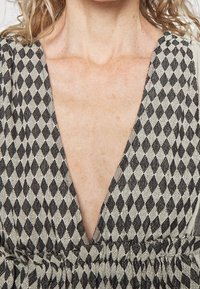Prenda de patrón negro y crema con un escote en V profundo y cintura fruncida. La tela presenta un diseño de diamante y una apariencia texturizada.
