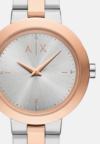 Ümar kell, millel on hõbedane tekstuuriga kelladial, roosa kuldne aktsent ja roostevabast terasest rihm. Omab minimalistlikke tunni markereid ja kristalldetaili.