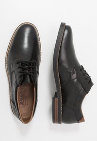 Scarpe da uomo in pelle nera con chiusura a lacci, punta tonda e un accento marrone sul tallone. Tessuto liscio e dettagli di cucitura minimi.