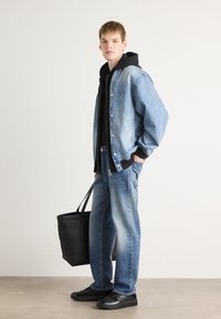 Chaqueta de mezclilla con herrajes plateados, sudadera azul y jeans de un azul claro. Un bolso tote negro y zapatos de charol negros complementan el conjunto.