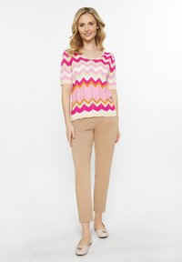 Top de punto con un patrón en zigzag rosa, blanco y naranja; mangas cortas; combinado con pantalones slim-fit beige y zapatos tipo slip-on de color beige claro.