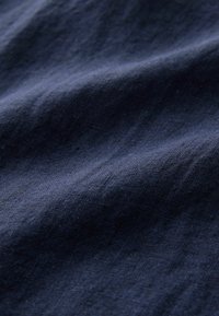 Tissu bleu foncé avec une texture visible et des plis subtils créant des ombres douces sur la surface.