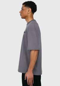 Graues Kurzarm-T-Shirt, oversized Passform, aus weichem Baumwollmaterial, mit dezent gesticktem Text auf der Vorderseite und Seitenschlitzen am Saum.