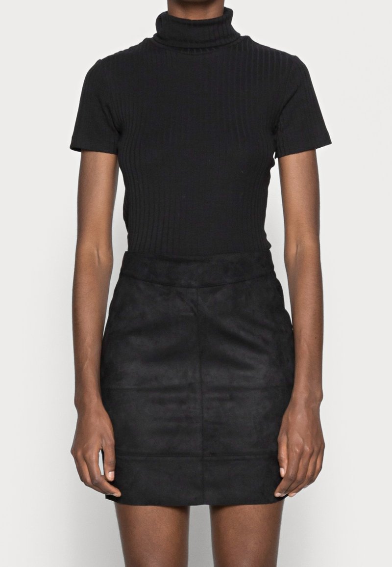 Maglione a collo alto nero a costine abbinato a una mini gonna in suede nera. Entrambi i capi presentano un design aderente e colori uniti senza fantasie.
