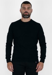 Maglione nero a maglia con maniche lunghe, scollo rotondo e orli a coste. Texture morbida e design aderente. Esibito su uno sfondo neutro.