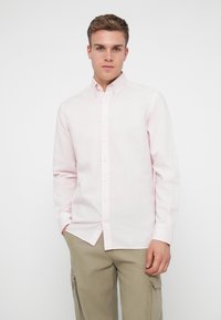 Camisa de botones rosa claro con cuello, mangas largas y dobladillo recto. La tela parece suave con una textura sutil.