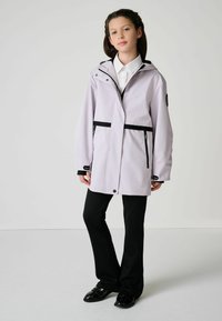 Svetlofialová pršiplášť s čiernymi akcentmi, predný zips, nastaviteľná kapucňa a dve vrecká na zips v kombinácii s čiernymi nohavicami a topánkami.