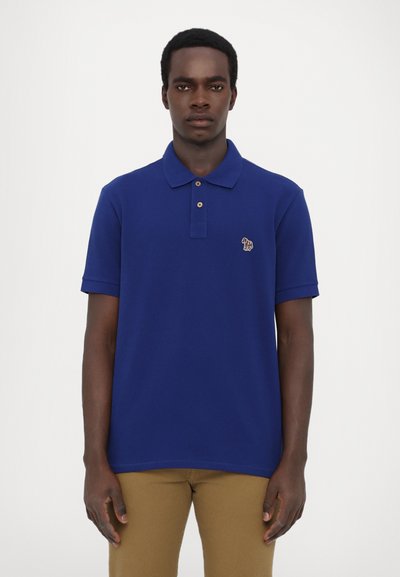 Maiou polo de culoare bleu marin, cu guler, mâneci scurte și trei nasturi maro. Prezintă un mic logo cu un elefant colorat pe pieptul stâng.