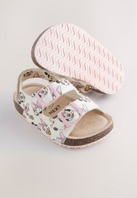 Sandales blanches avec un motif design comportant des personnages de dessin animé. Boucles réglables roses et semelle texturée rose et marron.