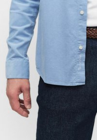 Lichtblauw overhemd met knopen van katoen, met een kraag en witte knopen, gecombineerd met donkere spijkerbroeken en een gevlochten bruine riem.