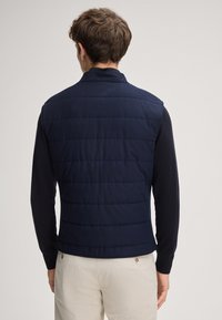 Granatowa pikowana kamizelka z wysokim kołnierzem, bez rękawów i gładką teksturą. Charakteryzuje się poziomym przeszyciem i dopasowanym krojem.